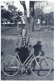 A copy of a black and white photograph of Muriel Darmody standing with her bicycle. The original photograph is from the 1940s. Muriel and Jim Darmody owned The Marysville Hotel in the 1950s.