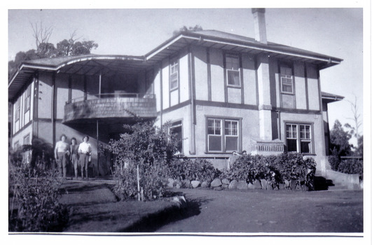 A black and white photograph taken at Mary Lodge Guest House in Marysville. The photograph was taken of three unknown people standing out the front of Mary Lodge. The photograph was taken in April 1944.