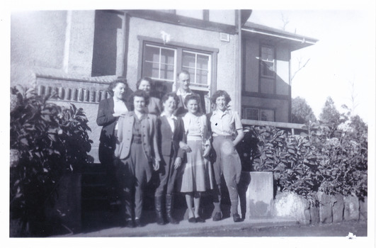 A black and white photograph taken at Mary Lodge Guest House in Marysville. The photograph was taken of a group of seven unknown people standing out the front of Mary Lodge. The photograph was taken in April 1944.