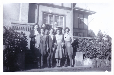 A black and white photograph taken at Mary Lodge Guest House in Marysville. The photograph was taken of a group of seven unknown people standing out the front of Mary Lodge. The photograph was taken in April 1944.