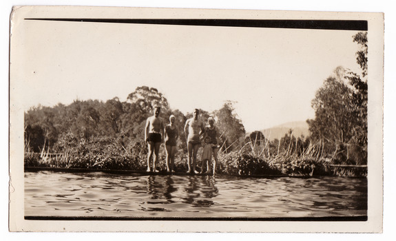 A black and white photograph taken at Mary Lodge Guest House in Marysville. The photograph is of a group of four unknown adults and a child standing on the edge of the swimming pool at Mary Lodge. The photograph was taken in 1941.