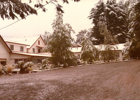 A copy of a sepia photograph taken at Kooringa Tourist House in Marysville. The photograph is of the main building and front garden at Kooringa after a light dusting of snow.