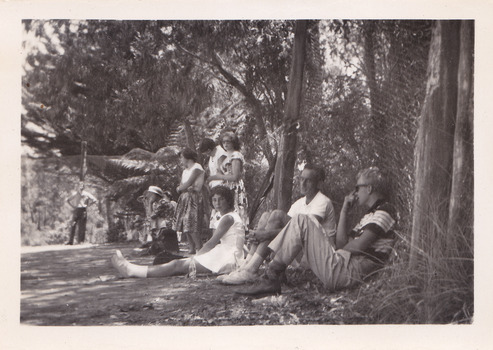 A black and white photograph taken at Mary-Lyn Guest House in Marysville. Mary-Lyn was a part of the Mary Chain of guest houses built by Eric Dowdle in the Depression years. The photograph is of an unknown group of people standing and sitting outside in the garden at Mary-Lyn.