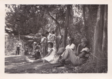 A black and white photograph taken at Mary-Lyn Guest House in Marysville. Mary-Lyn was a part of the Mary Chain of guest houses built by Eric Dowdle in the Depression years. The photograph is of an unknown group of people standing and sitting outside in the garden at Mary-Lyn.