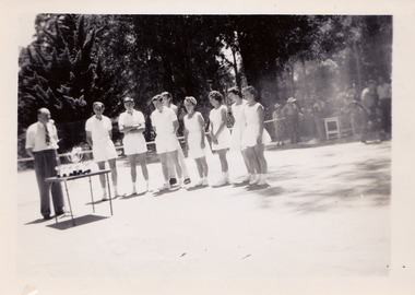 A black and white photograph taken at Mary-Lyn Guest House in Marysville. Mary-Lyn was a part of the Mary Chain of guest houses built by Eric Dowdle in the Depression years. The photograph is of an unknown man, possibly Mr. Fred Fiske the proprietor, presenting trophies to a group of people dressed in tennis outfits. The photograph was taken at the tennis court at Mary-Lyn.