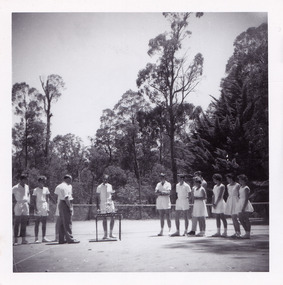 A black and white photograph that was taken at Mary-Lyn Guest House in Marysville. Mary-Lyn was a part of the Mary Chain of guest houses built by Eric Dowdle in the Depression years. The photograph is of an unknown man, possibly Mr. Fred Fiske the proprietor, presenting trophies to a group of people dressed in tennis outfits. The photograph was taken at the tennis court at Mary-Lyn.