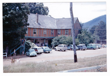 A copy of a colour photograph taken at Mary-Lyn Guest House in Marysville. Mary-Lyn was a part of the Mary Chain of guest houses built by Eric Dowdle in the Depression years. The photograph was taken in January 1964 and shows a view of the rear of the main building at Mary-Lyn. It also shows a large group of people who, according to an inscription on the reverse of the photograph, are watching a fire.