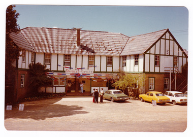 A colour photograph taken at Mary-Lyn Guest House in Marysville. Mary-Lyn was a part of the Mary Chain of guest houses built by Eric Dowdle in the Depression years. The photograph shows a view of the rear entrance of the main building with a banner above the door that says "Sterlings Tavern".