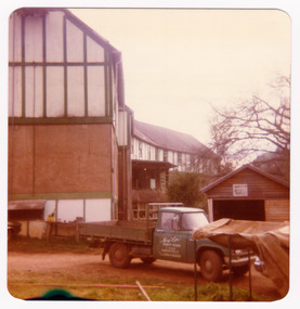 A colour photograph taken at Mary-Lyn Guest House in Marysville. Mary-Lyn was a part of the Mary Chain of guest houses built by Eric Dowdle during the Depression years. The photograph is of the front entrance with an old truck with the name "Mary-Lyn Guest House" on the side door in the foreground. The photograph was taken in 1979.