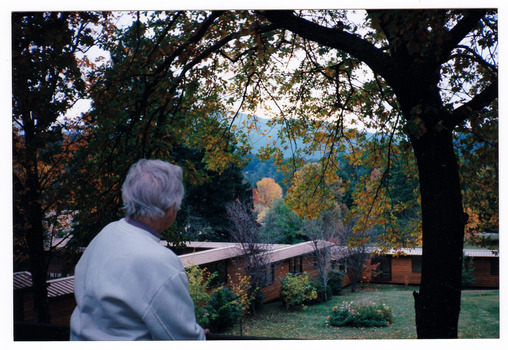 A colour photograph taken at Mary-Lyn Guest House in Marysville. Mary-Lyn was a part of the Mary Chain of guest houses built by Eric Dowdle during the Depression years. The photograph shows an unknown lady viewing the accommodation cabins that were built at Mary-Lyn.