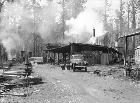 A copy of a black and white photograph of Cambarville township near Marysville. Cambarville was established as a timber mill town in the 1940s. Timber mill owners A. Cameron and F.J. Barton named Cambarville. They established the mill to salvage timber from trees destroyed in the 1939 bushfires. Cambarville was impacted by the 2009 Black Saturday bushfires and any remaining structures were destroyed. The original photograph was taken in April 1945.