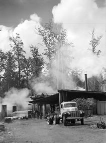 A digital copy of a black and white photograph of an old truck at the Cambarville timber mill near Marysville. Cambarville was established as a timber mill town in the 1940s. Timber mill owners A. Cameron and F.J. Barton named Cambarville. They established the mill to salvage timber from trees destroyed in the 1939 bushfires. Cambarville was impacted by the 2009 Black Saturday bushfires and any remaining structures were destroyed. The original photograph was taken in November 1945.