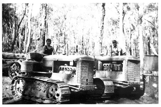 A copy of a black and white photograph of two Caterpillar crawler tractors with their drivers in the forest.