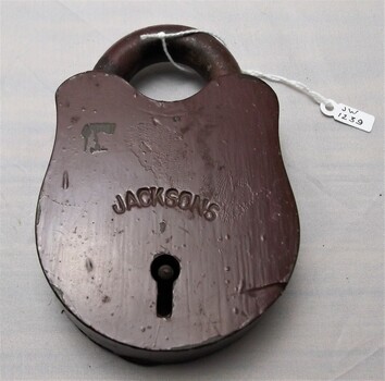 Brass padlock under brown paint with scraps and scratches. JACKSONS engraved across keyhole.