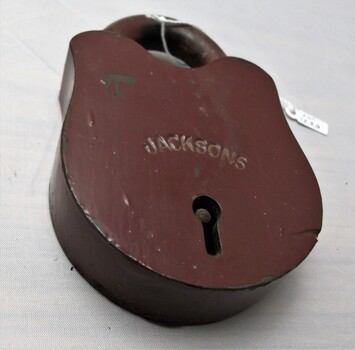Brass padlock under brown paint with scraps and scratches. JACKSONS engraved across keyhole.