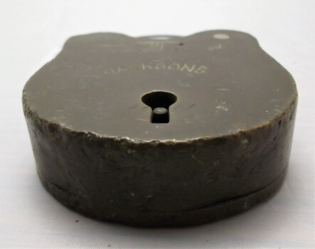 Bottom side view of a padlock with dents, keyhole, and engravings.