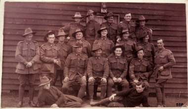 Group of 19 soldiers outside a hut.