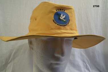Yellow floppy hat with Peace monitoring symbol on.