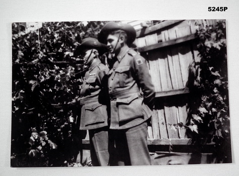 Photo of two soldiers standing against a wooden fence.