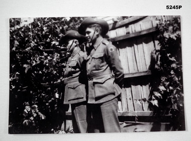 Photo of two soldiers standing against a wooden fence.