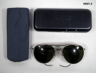 Aviator style flying spectacles with dark lens and contained in a metal case.