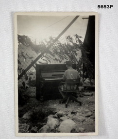 Photograph, man on a piano under Cam net.