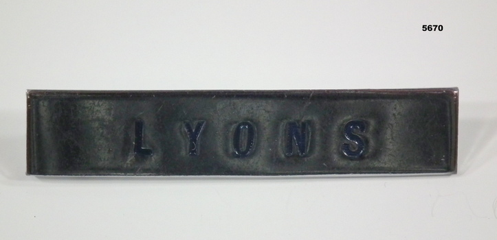 Rectangular silver coloured metal badge with blue lettering.