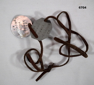 Set of tin identity discs on knotted brown leather cord. 