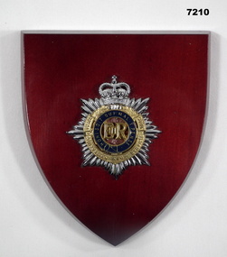 Plaque featuring a RAASC badge on a shield shaped wooden mount.