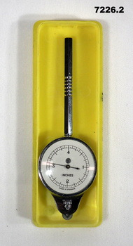 Circular metal instrument with small wheel and dial for measuring distance on a map.
