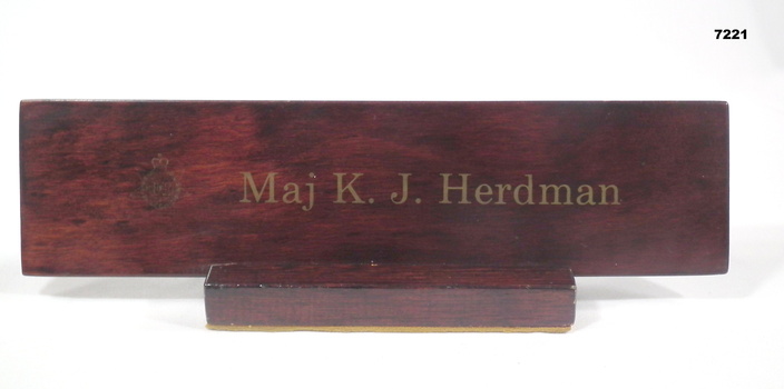 Brown coloured wooden name plaque with unit insignia and gold lettering.