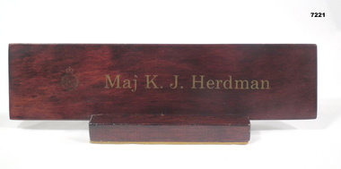 Brown coloured wooden name plaque with unit insignia and gold lettering.