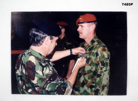 Coloured photograph of person pinning medal on a serviceman.