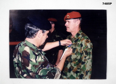 Coloured photograph of person pinning medal on a serviceman.