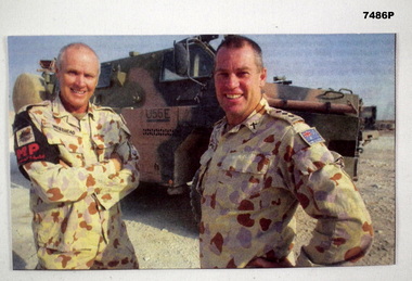 Coloured photo of two soldiers standing in front of an army vehicle.
