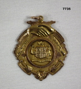 Gold coloured medallion with engraved details on back.