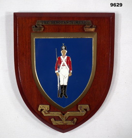 Shield shaped wooden plaque featuring an 18th Century soldier in uniform.