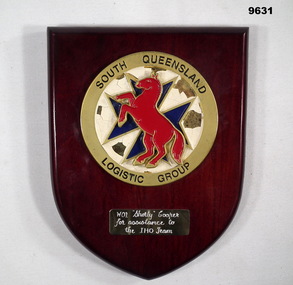 Shield shaped brown coloured wooden plaque with unit insignia.