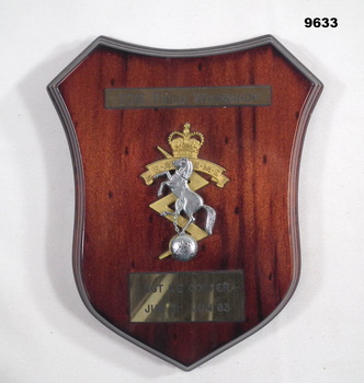 Shield shaped wooden plaque with unit insignia.