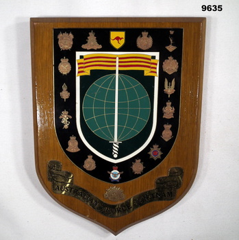 Shield shaped wooden plaque featuring Vietnam era army insignia.