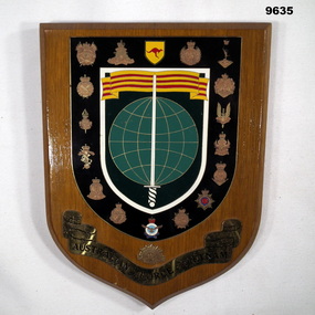 Shield shaped wooden plaque featuring Vietnam era army insignia.