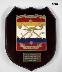 Shield shaped wooden plaque with unit insignia and name plate.