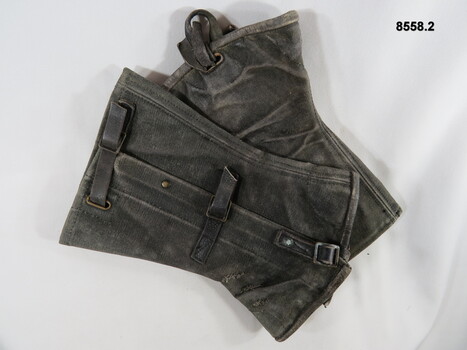 Blackened gaiters, worn around ankles with brass buckles and leather straps.
