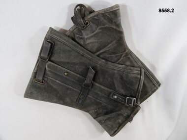 Blackened gaiters, worn around ankles with brass buckles and leather straps.