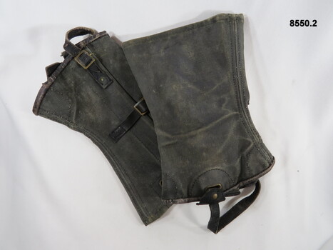 Blackened gaiters, worn around ankles with brass buckles and leather straps.