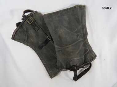 Blackened gaiters, worn around ankles with brass buckles and leather straps.