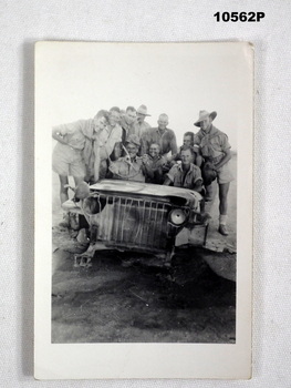 Photograph of a group of Australian soldiers in uniform, standing around a wrecked jeep.
