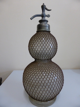 This is aglass soda syphon with anet metal covering.