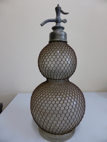 This is aglass soda syphon with anet metal covering.