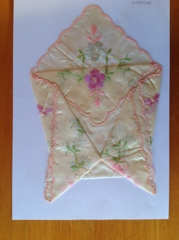 This is a cream silk hankerchief which is embroidered with different shaded pink flowers and green foliage.